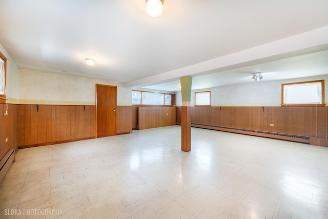 basement featuring a baseboard radiator, wainscoting, light flooring, and wooden walls