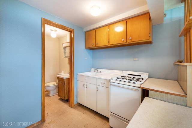 kitchen with white gas stove, wallpapered walls, a sink, light countertops, and baseboards