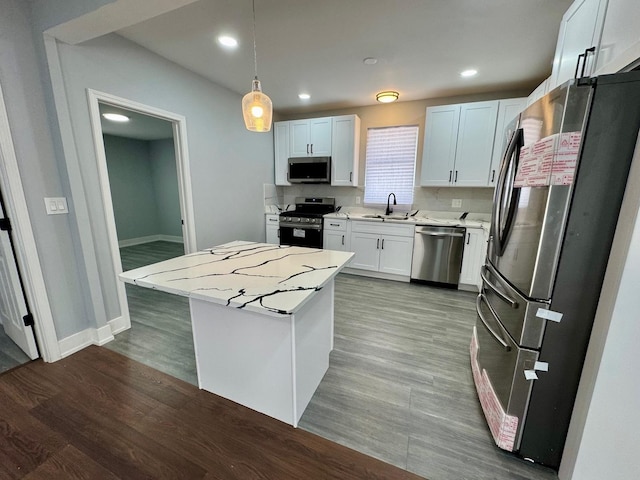 kitchen with appliances with stainless steel finishes, a sink, light countertops, a kitchen island, and wood finished floors
