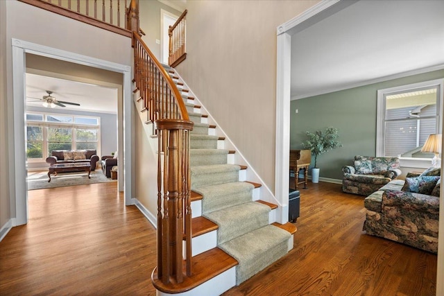 stairs with wood finished floors, baseboards, ceiling fan, and ornamental molding