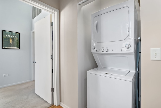 washroom featuring stacked washer / dryer, baseboards, and light colored carpet