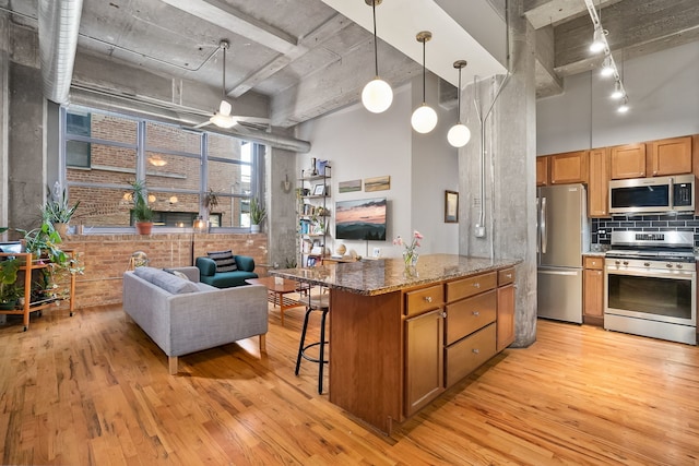 kitchen with appliances with stainless steel finishes, a high ceiling, light wood-style flooring, a kitchen breakfast bar, and brown cabinets