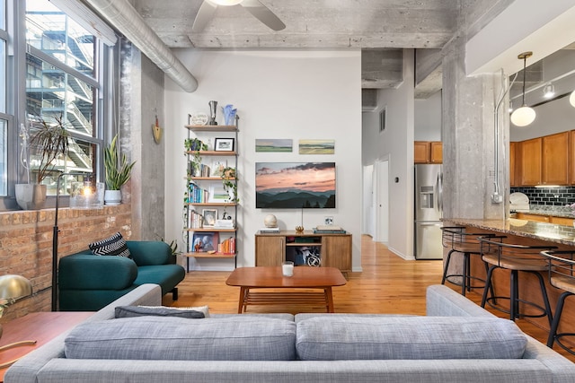 living room with light wood-style floors, a ceiling fan, and a towering ceiling