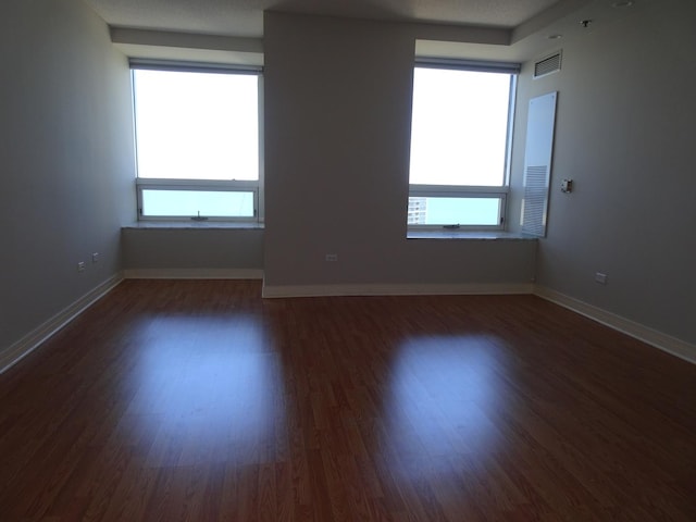 unfurnished room featuring healthy amount of natural light, wood finished floors, and baseboards