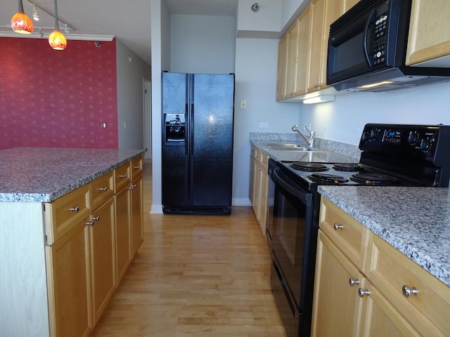 kitchen featuring black appliances, a sink, an accent wall, wallpapered walls, and light wood finished floors