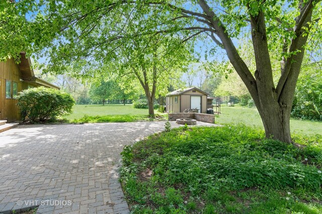 view of green lawn with an outbuilding, a patio, and a fire pit