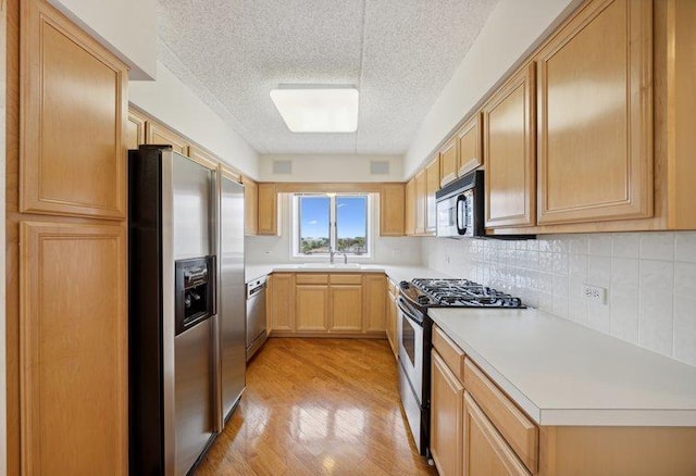 kitchen with appliances with stainless steel finishes, a sink, a textured ceiling, light countertops, and light brown cabinetry