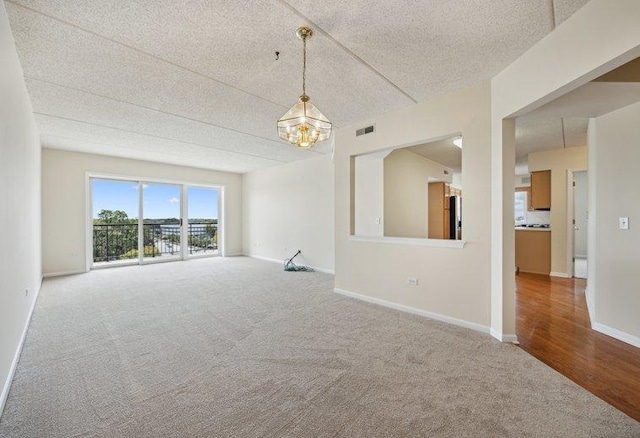 spare room featuring carpet floors, a textured ceiling, a chandelier, and baseboards