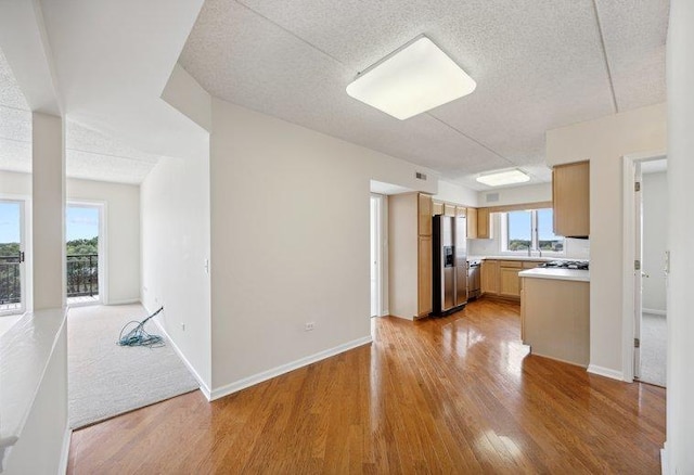 kitchen with light wood-style flooring, stainless steel fridge, light countertops, a textured ceiling, and baseboards