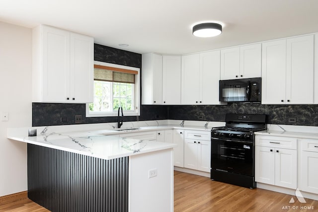 kitchen with black appliances, a sink, a peninsula, light wood finished floors, and white cabinetry