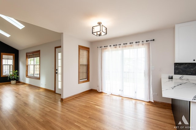 unfurnished dining area with light wood-type flooring, baseboards, a skylight, and lofted ceiling