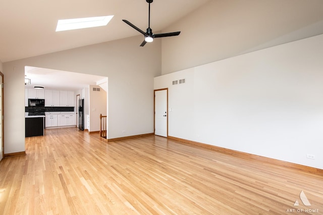 unfurnished living room with a skylight, high vaulted ceiling, light wood finished floors, a ceiling fan, and baseboards