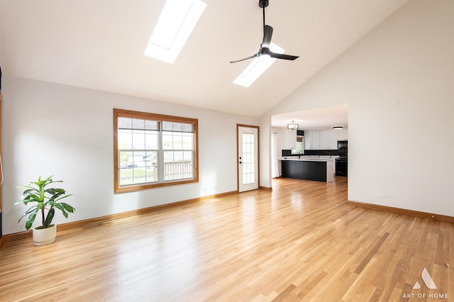 unfurnished living room with a skylight, high vaulted ceiling, light wood-style floors, a ceiling fan, and baseboards