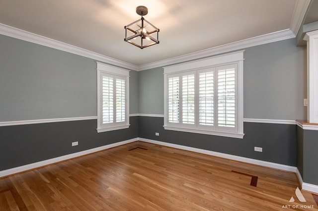 spare room featuring plenty of natural light, a chandelier, baseboards, wood finished floors, and crown molding