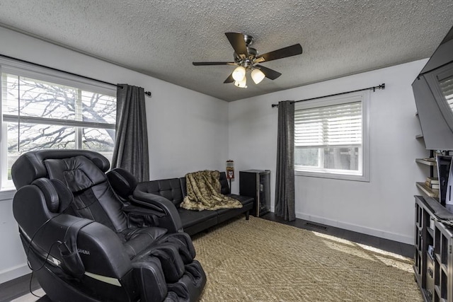 living room with a textured ceiling, a ceiling fan, baseboards, and wood finished floors