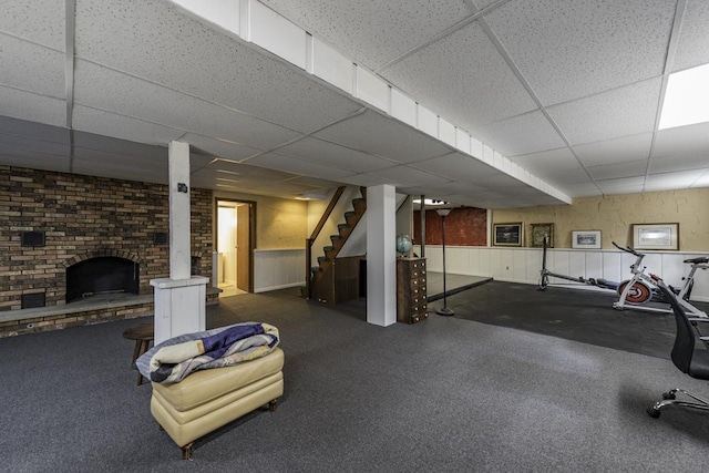 finished below grade area featuring a paneled ceiling, stairway, wainscoting, and a fireplace