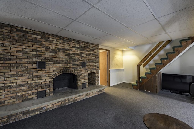 unfurnished living room featuring a paneled ceiling, carpet flooring, stairway, a brick fireplace, and baseboards