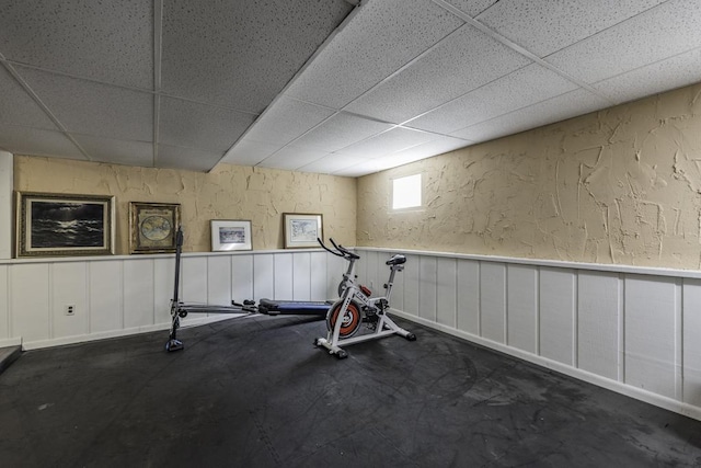 exercise area with a paneled ceiling and a wainscoted wall