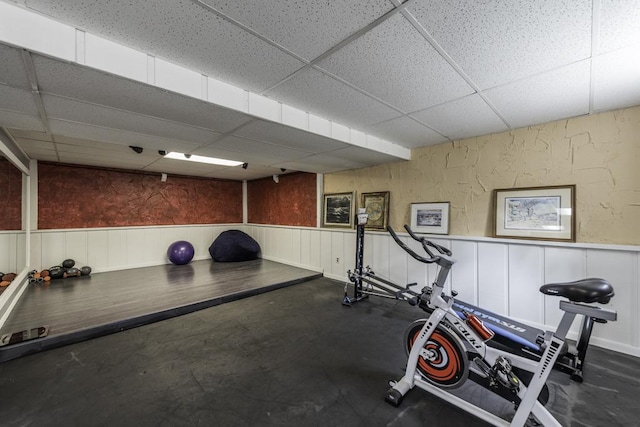 workout room featuring a paneled ceiling and wainscoting