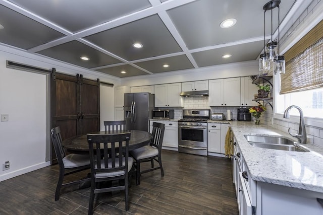 kitchen with appliances with stainless steel finishes, a sink, a barn door, under cabinet range hood, and coffered ceiling
