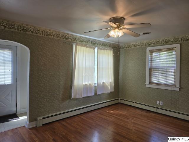 301 N St, Augusta, IL 62311 - empty room featuring wood finished floors, arched walkways, ceiling fan, and a baseboard radiator