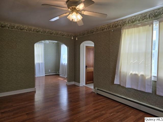 301 N St, Augusta, IL 62311 - empty room featuring baseboard heating, arched walkways, wood finished floors, and wallpapered walls