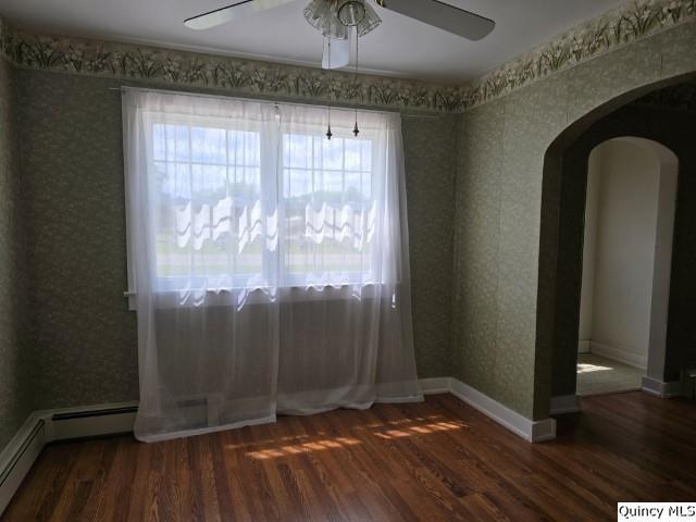 301 N St, Augusta, IL 62311 - spare room featuring ceiling fan, arched walkways, wood finished floors, a baseboard radiator, and wallpapered walls