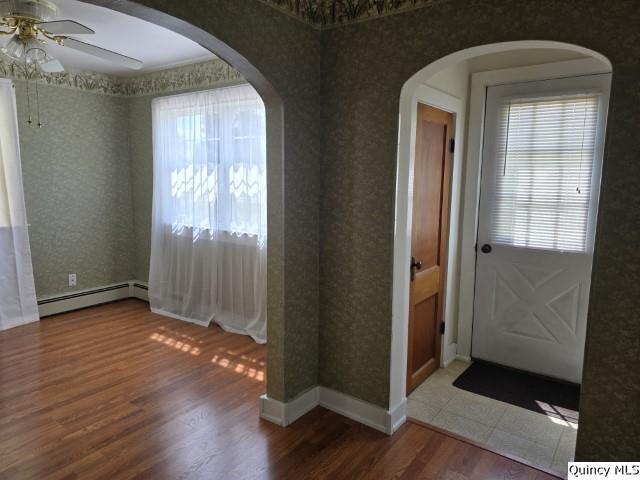 301 N St, Augusta, IL 62311 - unfurnished room featuring a baseboard heating unit, a ceiling fan, wallpapered walls, wood finished floors, and arched walkways