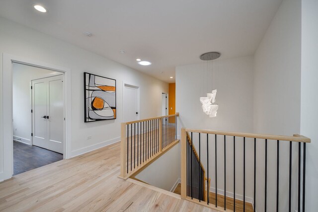 corridor with an upstairs landing, wood finished floors, recessed lighting, and baseboards