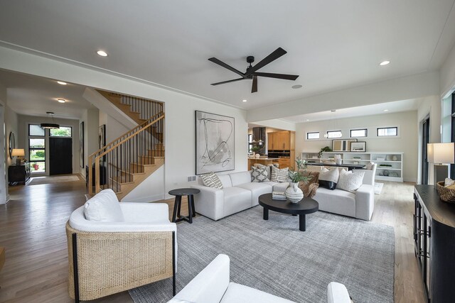 living room with healthy amount of natural light, wood finished floors, ceiling fan, stairway, and recessed lighting