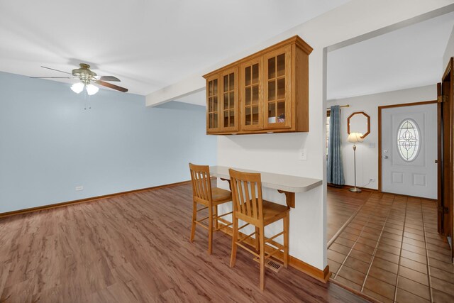 588 Renee Dr, South Elgin, IL 60177 - kitchen featuring ceiling fan, brown cabinets, a kitchen breakfast bar, glass insert cabinets, and baseboards