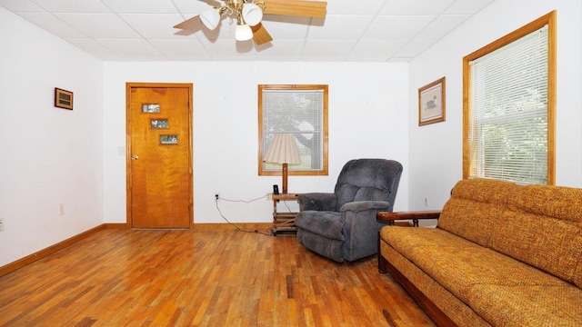 living area featuring a drop ceiling, wood finished floors, ceiling fan, and baseboards