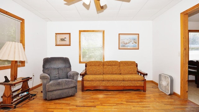 living area with a drop ceiling, ceiling fan, light wood-style flooring, and baseboards