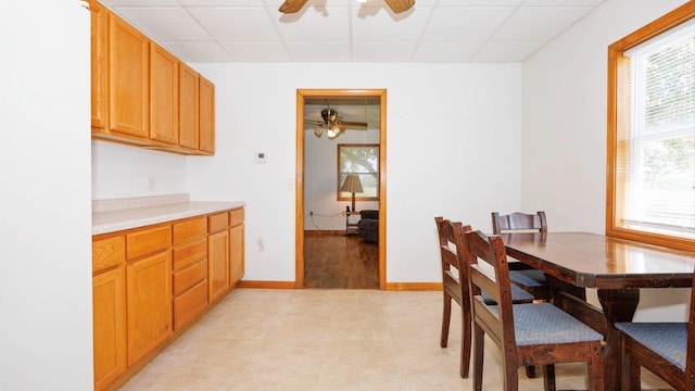 dining area with a ceiling fan, plenty of natural light, a paneled ceiling, and baseboards