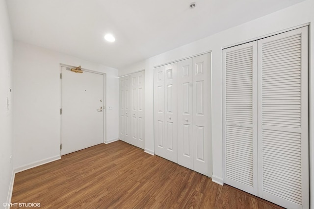 unfurnished bedroom with two closets, wood finished floors, baseboards, and recessed lighting