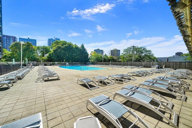 community pool with a patio area, fence, and a city view