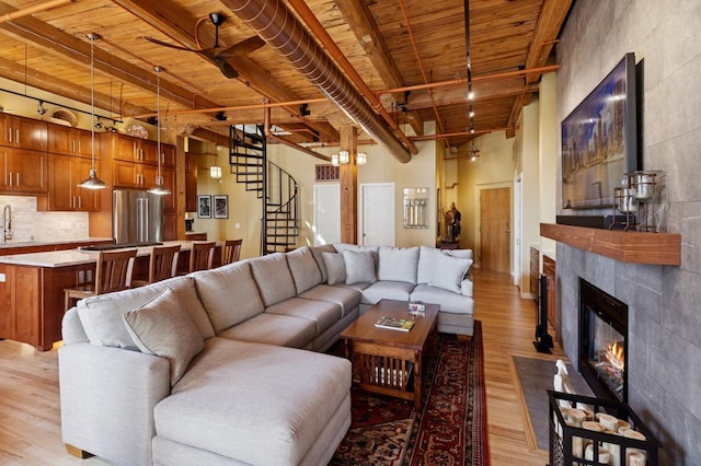 living room with wooden ceiling, light wood-style flooring, beam ceiling, stairway, and a tile fireplace