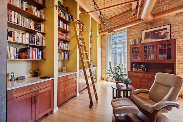 living area featuring brick wall, light wood-style floors, and a high ceiling