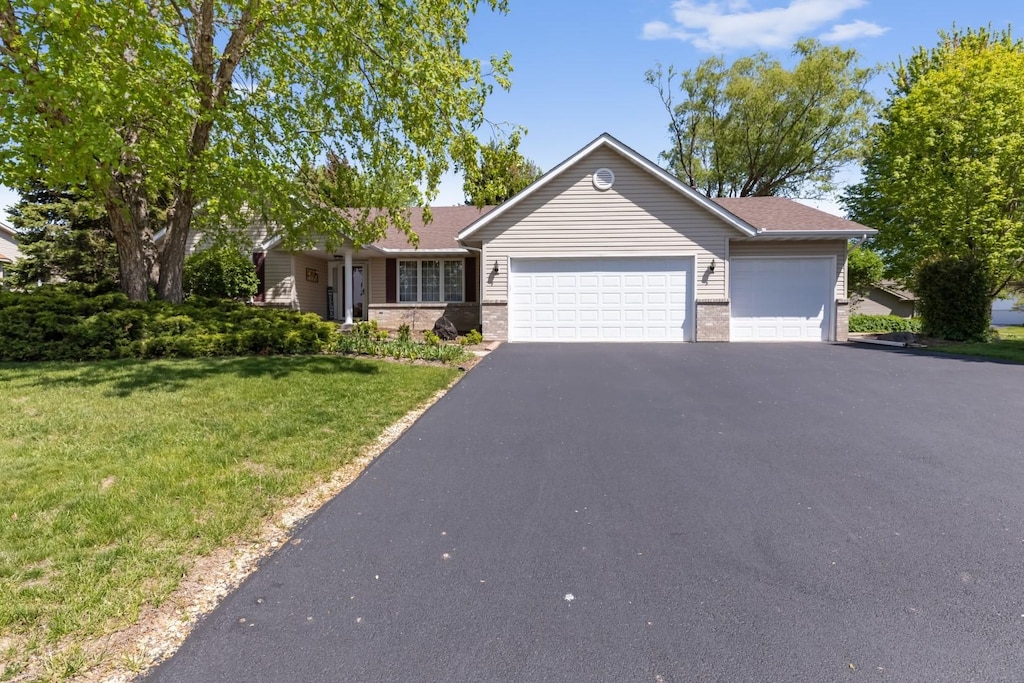 ranch-style home with a garage, brick siding, driveway, and a front yard