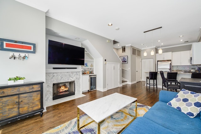living room with wine cooler, ornamental molding, dark wood-style flooring, a high end fireplace, and recessed lighting