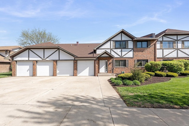 tudor-style house featuring concrete driveway, brick siding, a garage, and a front yard