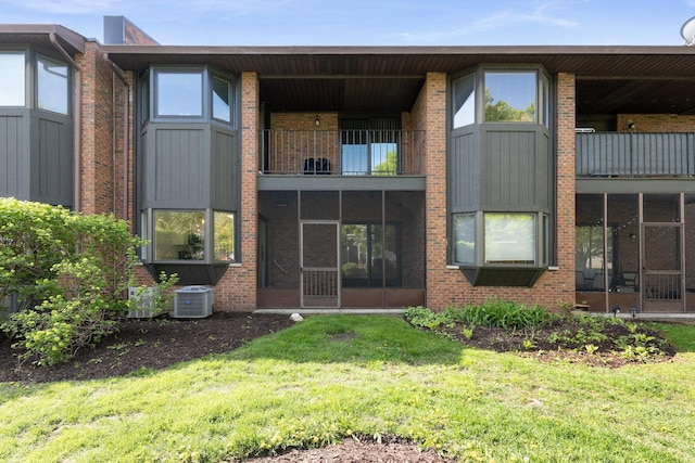 rear view of house with central AC, a yard, and brick siding