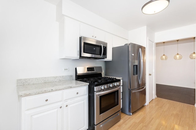 kitchen featuring stainless steel appliances, light wood-style floors, white cabinets, light stone countertops, and decorative light fixtures