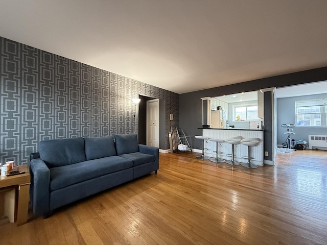 living area featuring radiator, wallpapered walls, wood finished floors, an accent wall, and baseboards