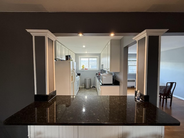 kitchen with white fridge with ice dispenser, radiator heating unit, light wood-style flooring, dark stone counters, and a peninsula
