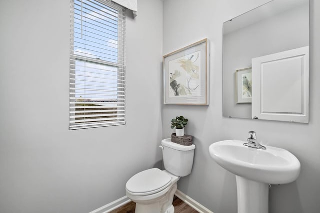 half bath featuring wood finished floors, baseboards, toilet, and a sink
