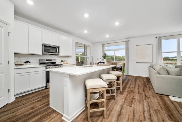 kitchen with appliances with stainless steel finishes, dark wood finished floors, a breakfast bar, an island with sink, and recessed lighting