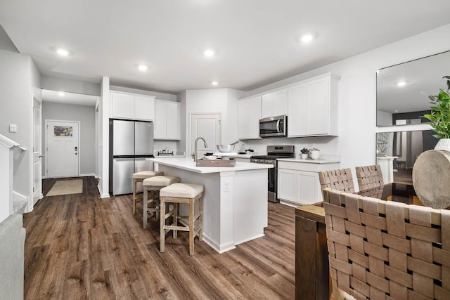 kitchen with stainless steel appliances, dark wood-style floors, an island with sink, a kitchen breakfast bar, and white cabinetry