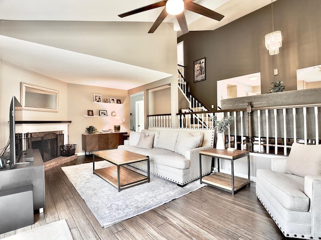 living room with a ceiling fan, high vaulted ceiling, wood finished floors, a stone fireplace, and stairway