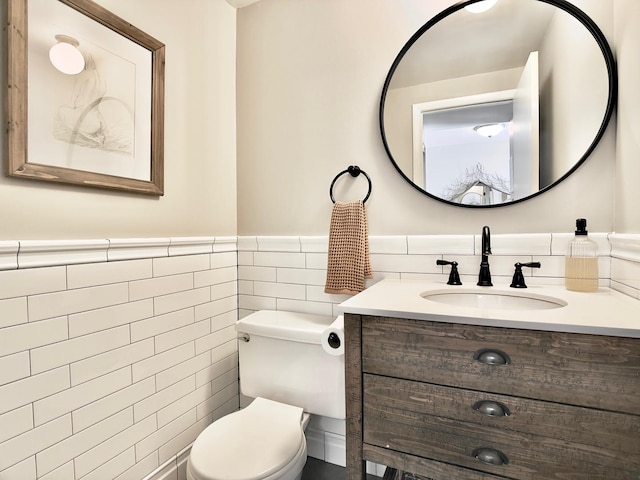 bathroom with tile walls, wainscoting, toilet, and vanity